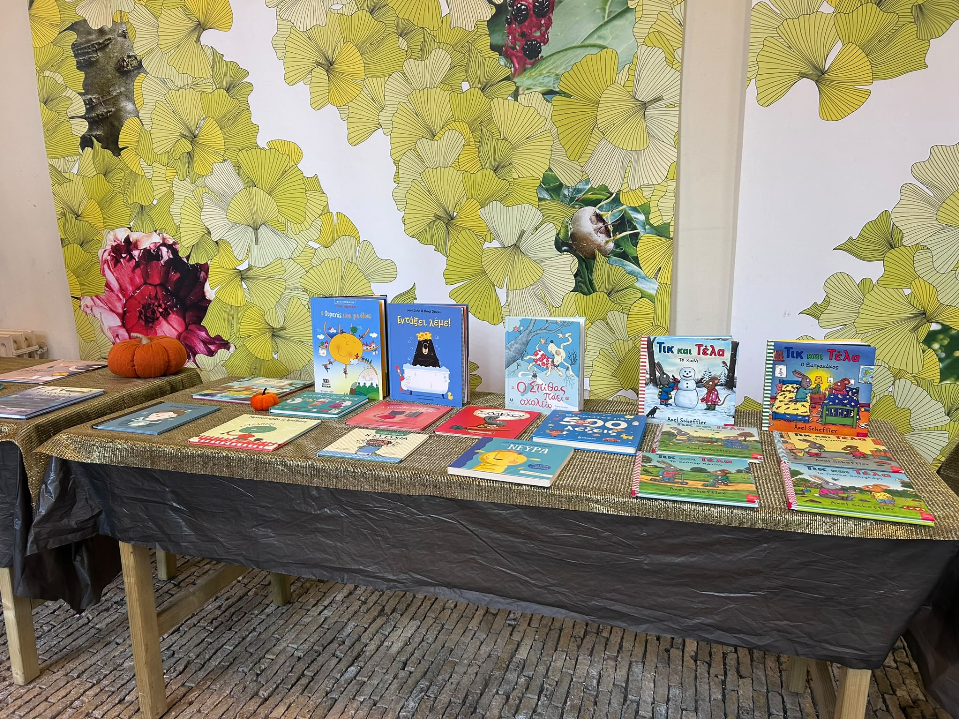 Greek and English children's books displayed on a gold table cloth at the book swap.
